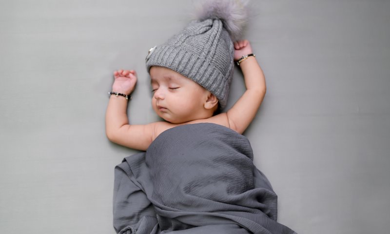 Ein schlafendes Baby mit Wollmütze und grauer dünner Decke