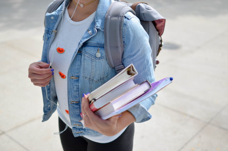 Schulmädchen mit Büchern auf dem Arm und Schulrucksack auf dem Rücken