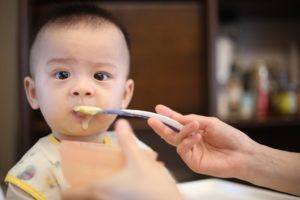 Kind isst Brei mit Löffel und schaut zweifelnd