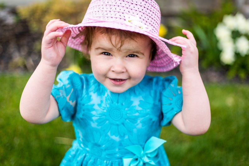 Ein lachendes Mädchen mit pinkem Sonnenhut und blauem Kleid Ein lachendes Mädchen mit pinkfarbenem Sonnenhut