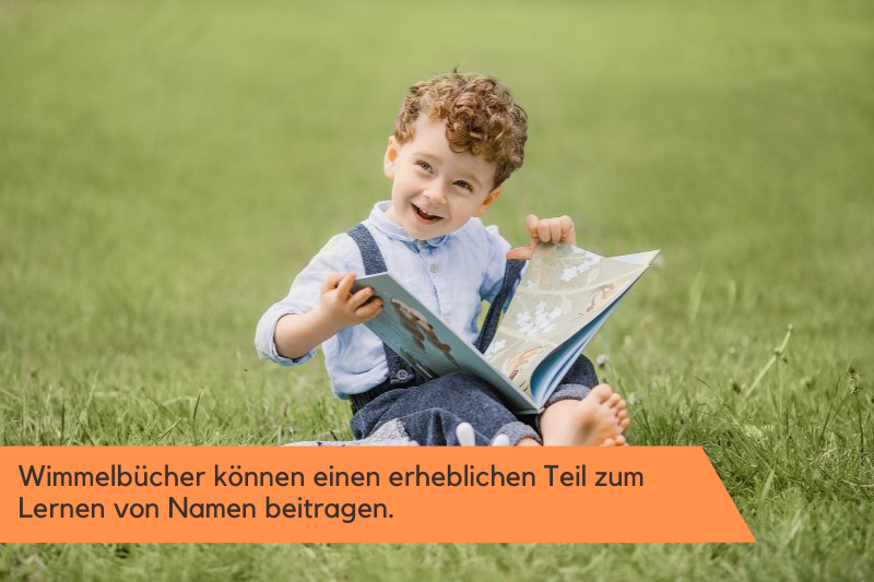 Ein kleiner Junge sitzt mit einem Wimmelbuch auf einer Wiese.