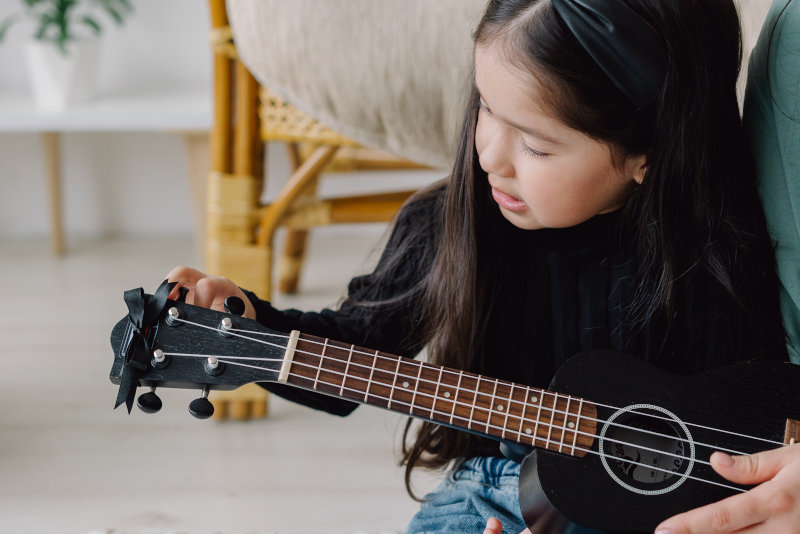 Kind lernt das Spielen auf einer Kinder-Ukulele Ein Kind lernt das Ukulele spielen