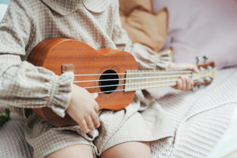 Kinderinstrumente: Ein Kind, das auf einer Kinder-Ukulele spielt.