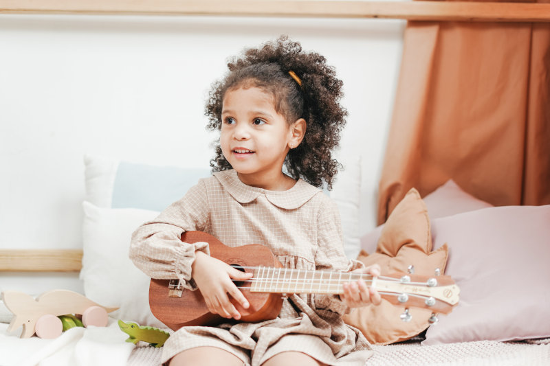 Kleines Kind spielt auf einer Ukulele für Kinder Ein kleines Mädchen spielt zufrieden auf einer Kinder-Ukulele