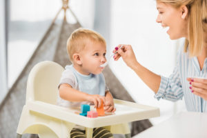 Kind im Hochstuhl, das gefüttert wird von der Mutter