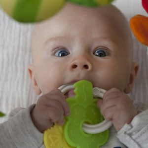 Baby mit Babyrassel in den Mund
