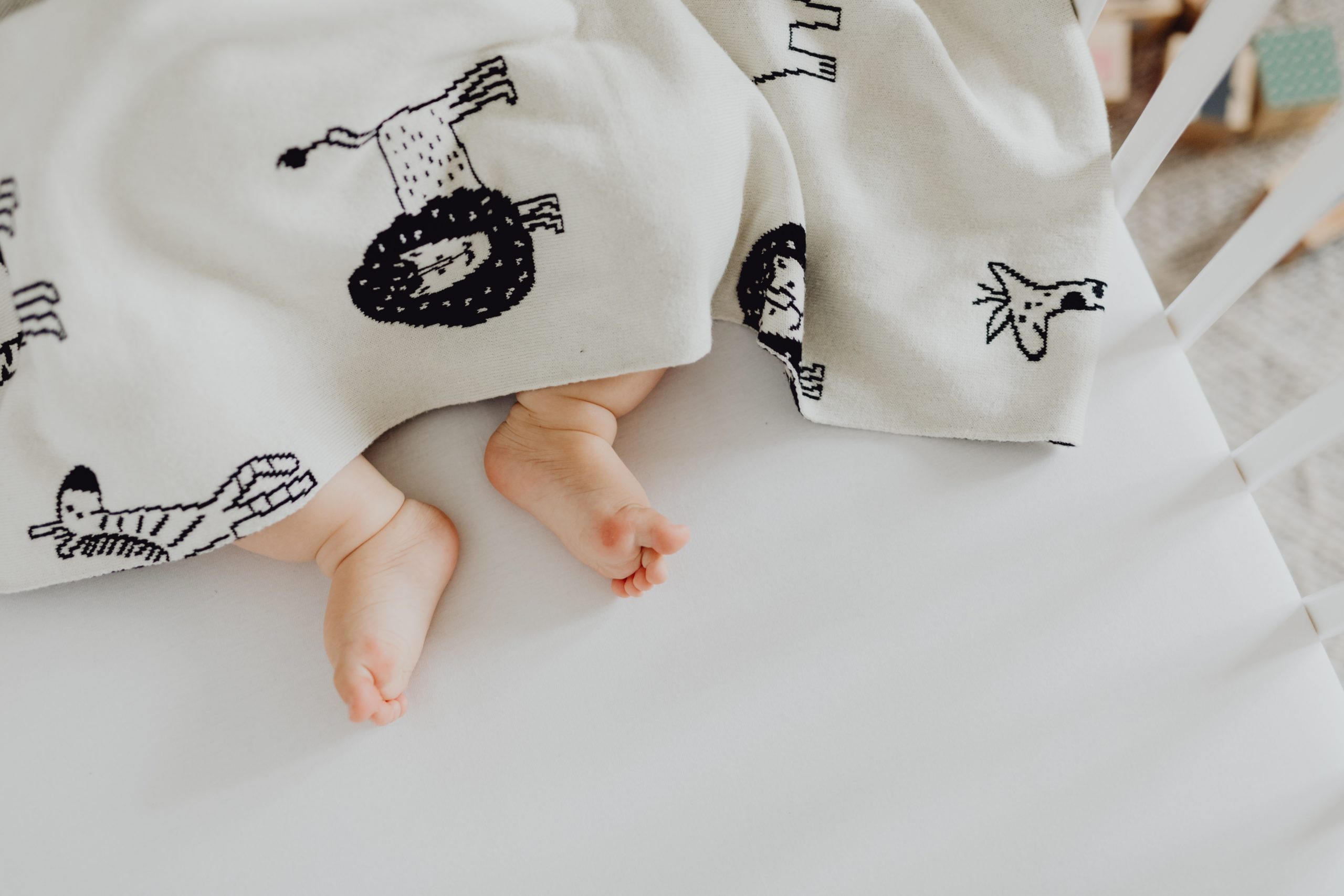 Babyfüße sind mit einer Babydecke zugedeckt Babyfüße schauen unter einer Babydecke heraus.