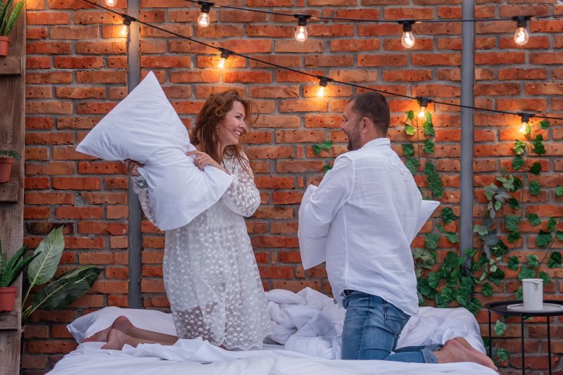 Paar hat Kissenschlacht im Bett mit Daunenkissen Kissenschlacht mit Kopfkissen