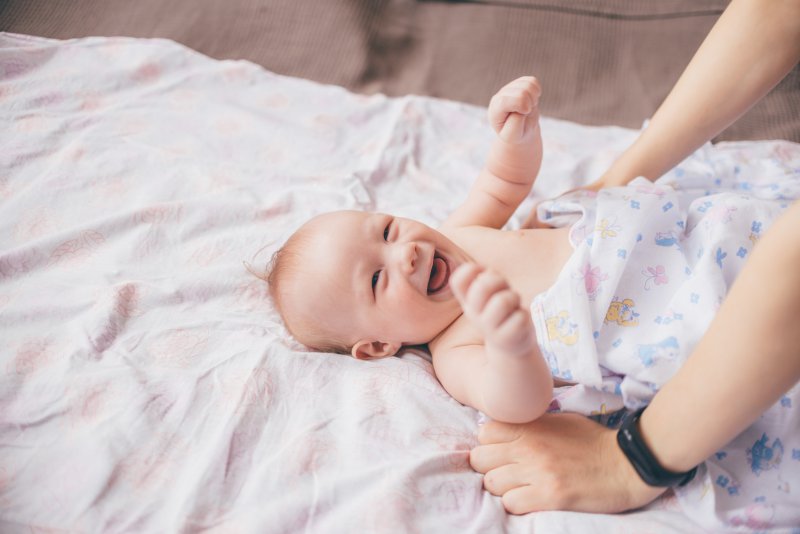 Baby liegt auf Matratze und lacht.