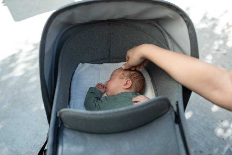 Ein Neugeborenes schläft in einem grauen Sommerfußsack, mit abnehmbarem Oberteil. Ein Neugeborenes schläft in einem grauen Sommerfußsack