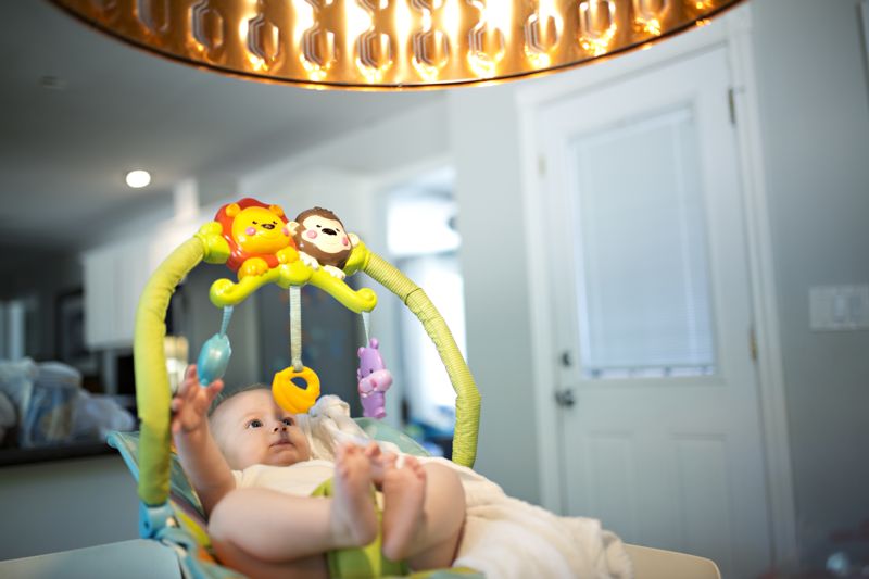 Baby spielt mit Spielbogen Baby in Babywippe mit Spielbogen