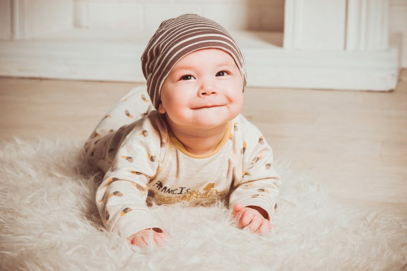 Ein Baby trägt einen beigen Strampelanzug und ein braunes Mützchen, perfekt für den Fußsack vorbereitet. Ein lächelndes Baby mit einem beigen Strampelanzug und einer braun weiß gestreiften Mütze