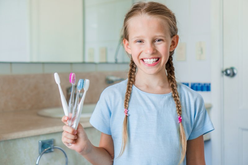 elektrische-zahnbuerste-fuer-Kinder-test Lächelndes Mädchen hält mehrere Handzahnbürsten in der Hand.