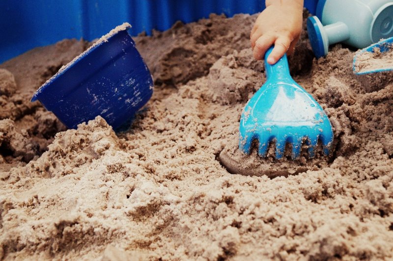Spielen im Sandkasten Kinderhand spielt im Sand mit einer Hake